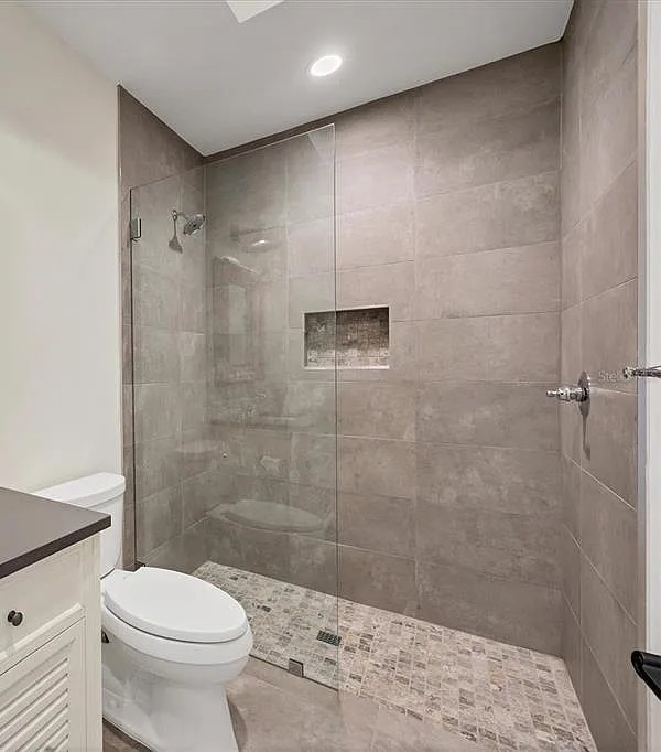 Walk-in shower with large-format gray porcelain tile, mosaic floor and glass panel in Sarasota, FL