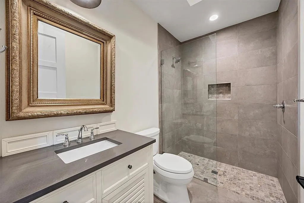 Remodeled bathroom with a large-format porcelain tile walk-in shower, mosaic floor, quartz-top vanity and framed mirror in Sarasota, FL
