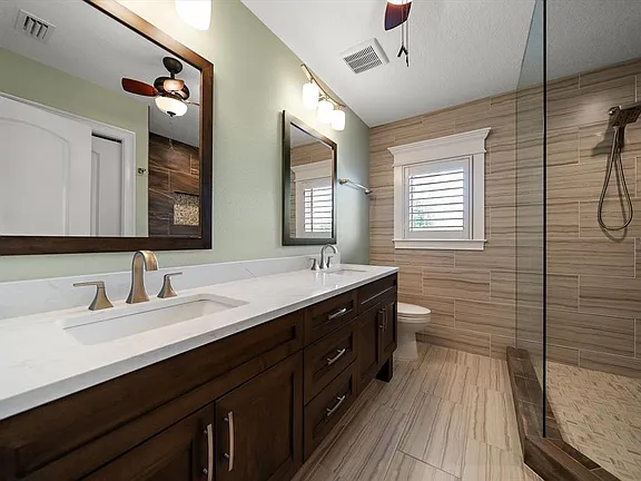 Remodeled beach-home bathroom with wood-look porcelain tile walk-in shower, double vanity with quartz top and dark wood cabinetry in St. Pete Beach, FL